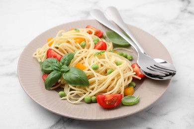 Plate of delicious pasta primavera and cutlery on white marble table, closeup