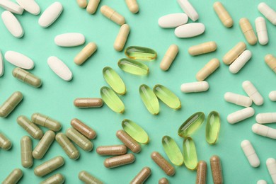 Photo of Different vitamin capsules on turquoise background, top view