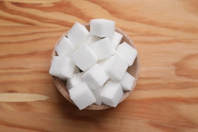 Photo of White sugar cubes in bowl on wooden table, top view