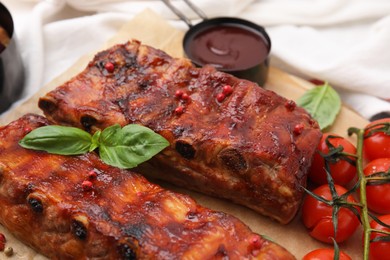 Photo of Tasty roasted pork ribs served with sauce, basil and tomatoes on table, closeup