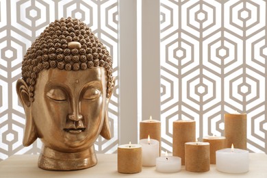 Buddha statue and burning candles on table indoors