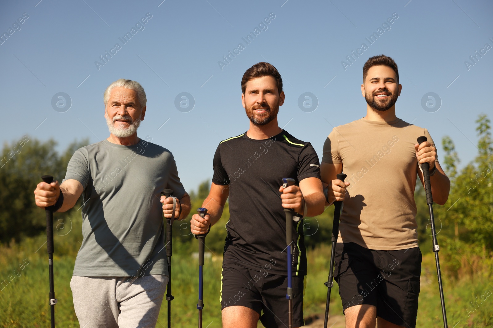Photo of Happy men practicing Nordic walking with poles outdoors on sunny day