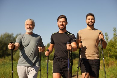 Happy men practicing Nordic walking with poles outdoors on sunny day