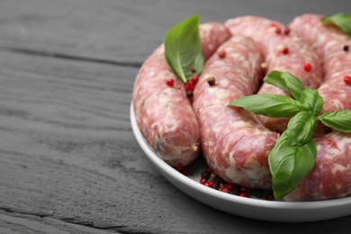 Photo of Raw homemade sausages, basil leaves and peppercorns on grey wooden table, closeup. space for text