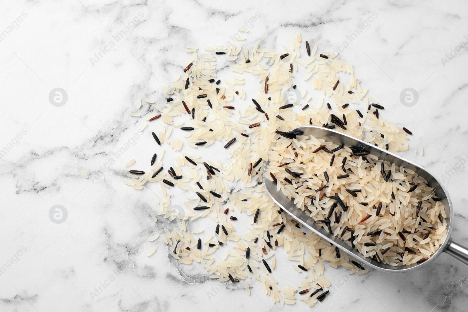 Photo of Mix of brown and polished rice with scoop on white marble table, top view