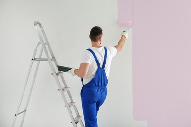 Man painting wall with light pink dye indoors, back view