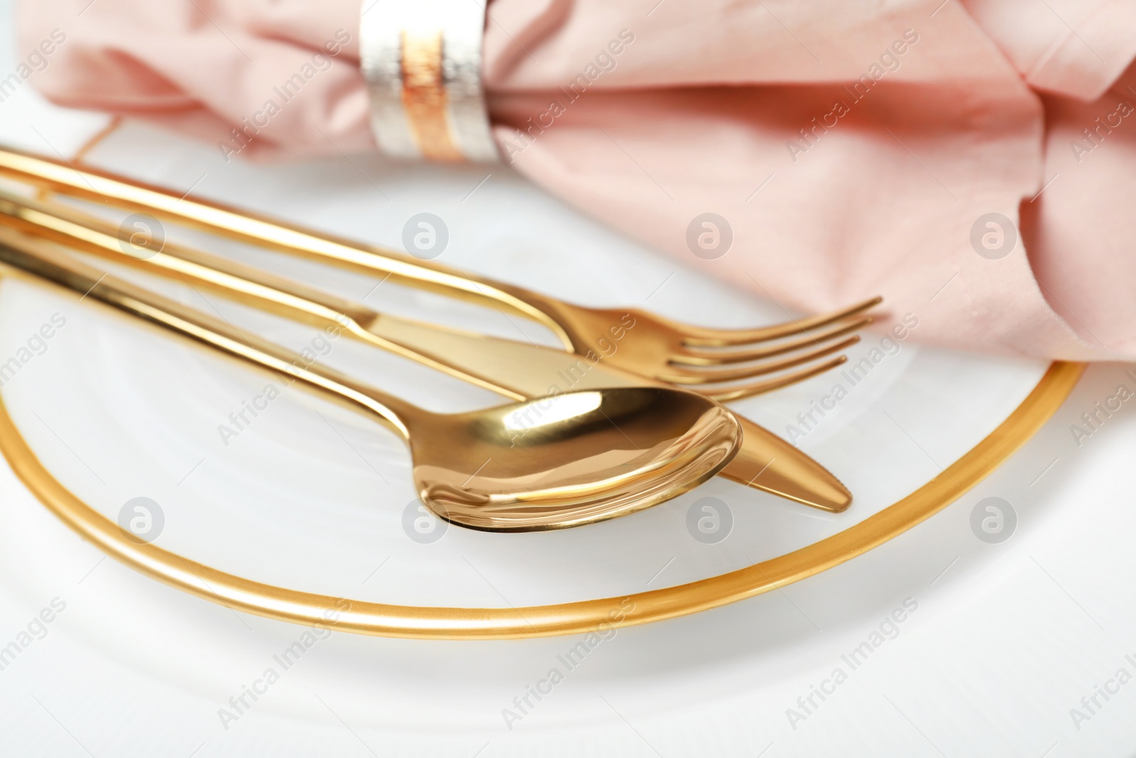 Photo of Plate with golden cutlery and napkin on table, closeup. Festive dinner setting