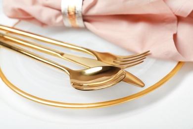 Photo of Plate with golden cutlery and napkin on table, closeup. Festive dinner setting