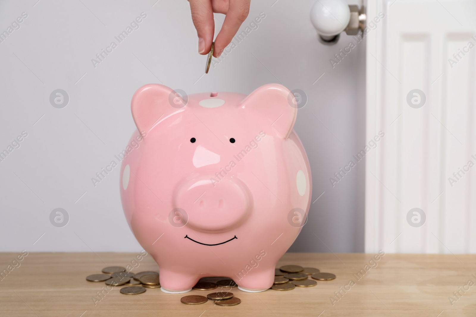 Photo of Woman putting coin into piggy bank near heating radiator, closeup