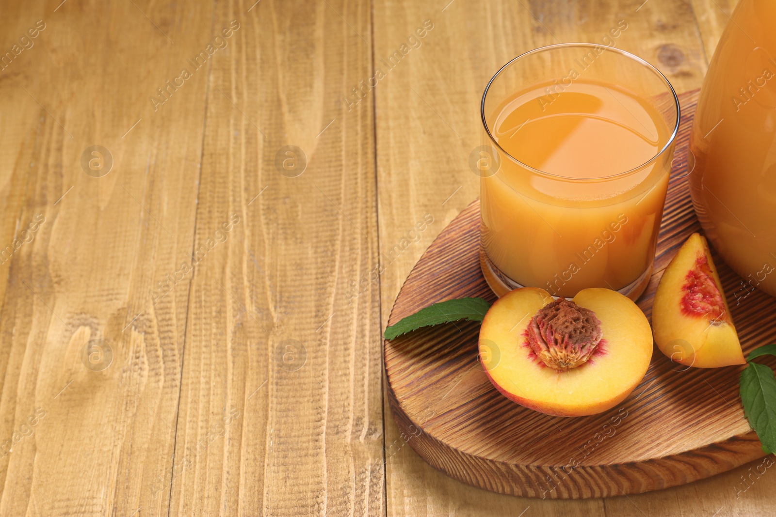 Photo of Delicious peach juice, fresh fruit and leaves on wooden table. Space for text