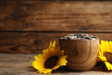 Photo of Raw sunflower seeds and flowers on wooden table. Space for text