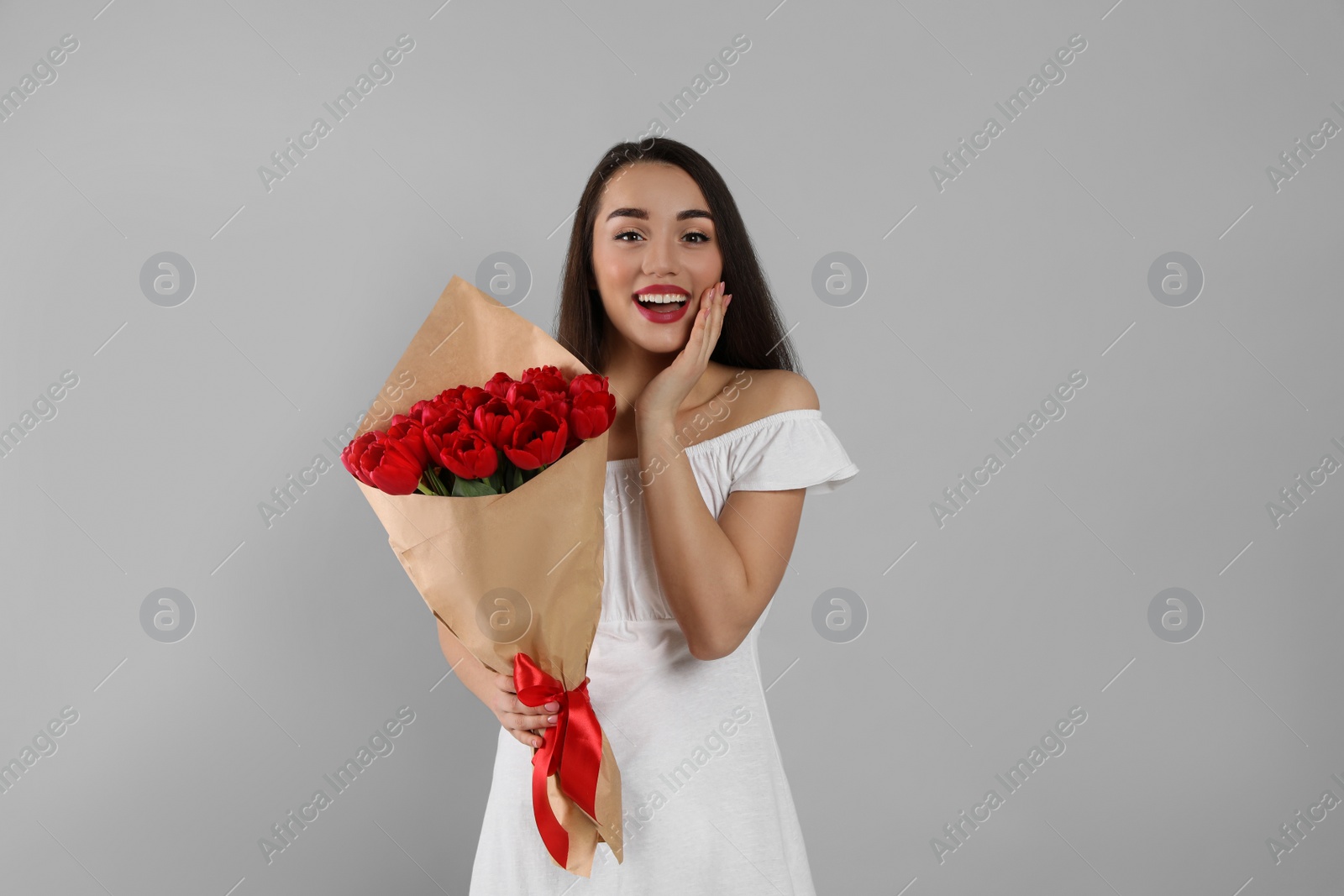 Photo of Happy woman with red tulip bouquet on light grey background. 8th of March celebration