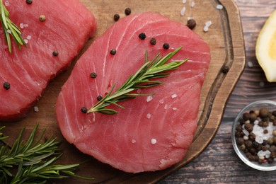 Photo of Raw tuna fillets with rosemary and peppercorns on wooden board, top view