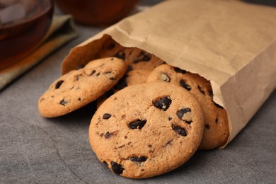 Photo of Paper bag with delicious chocolate chip cookies and tea on grey table, closeup