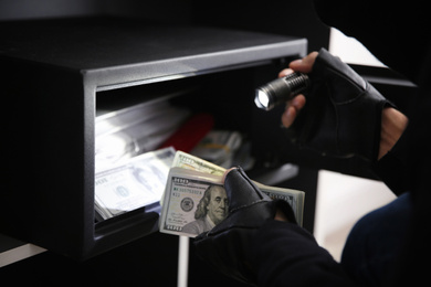 Thief taking money out of steel safe indoors, closeup