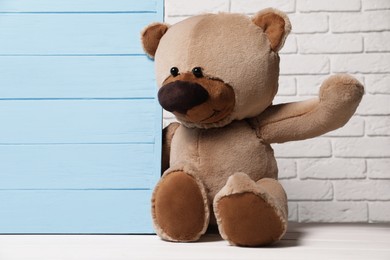Cute teddy bear near light blue wooden wall against brick background, space for text