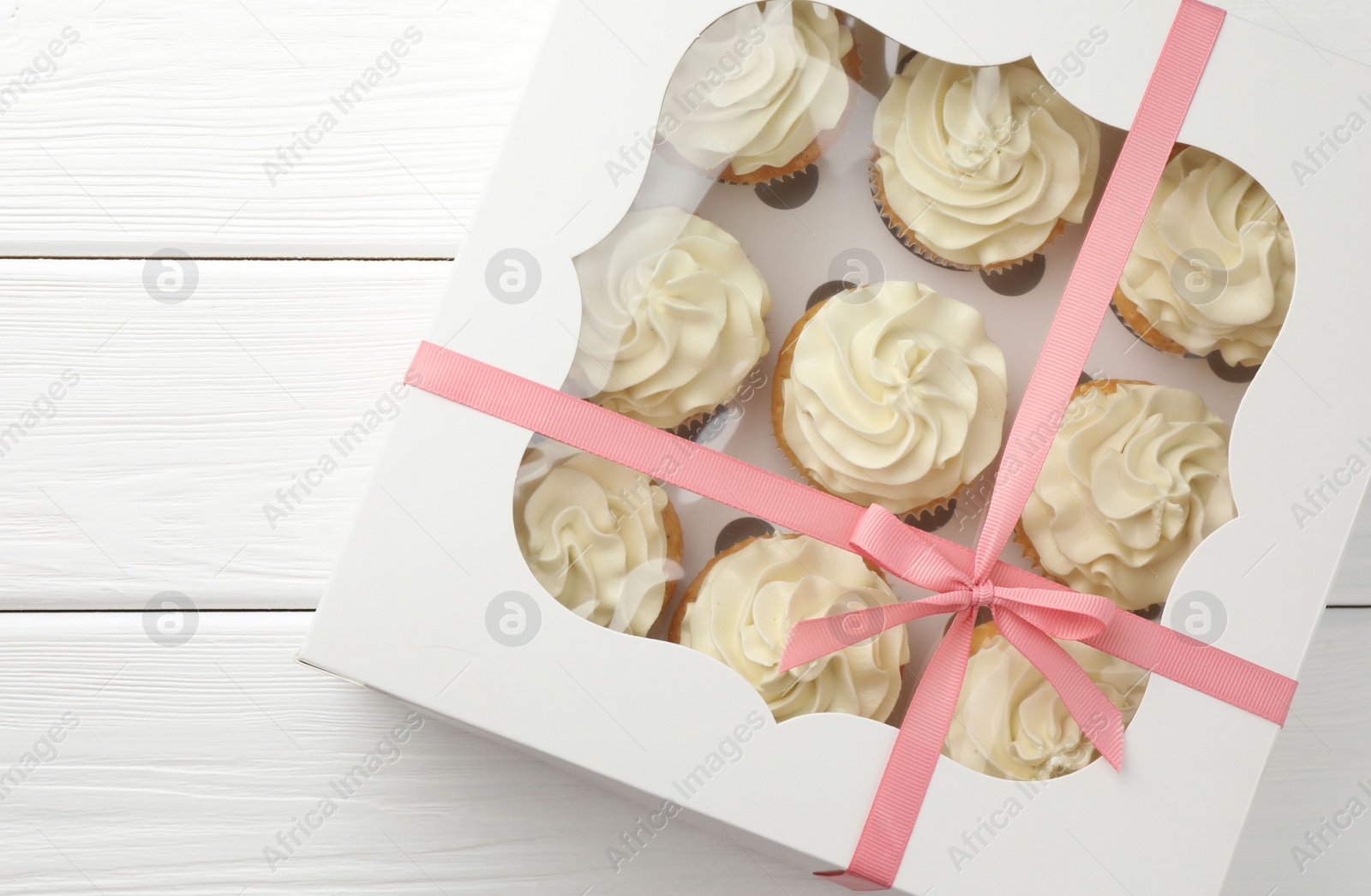 Photo of Tasty cupcakes with vanilla cream in box on white wooden table, top view