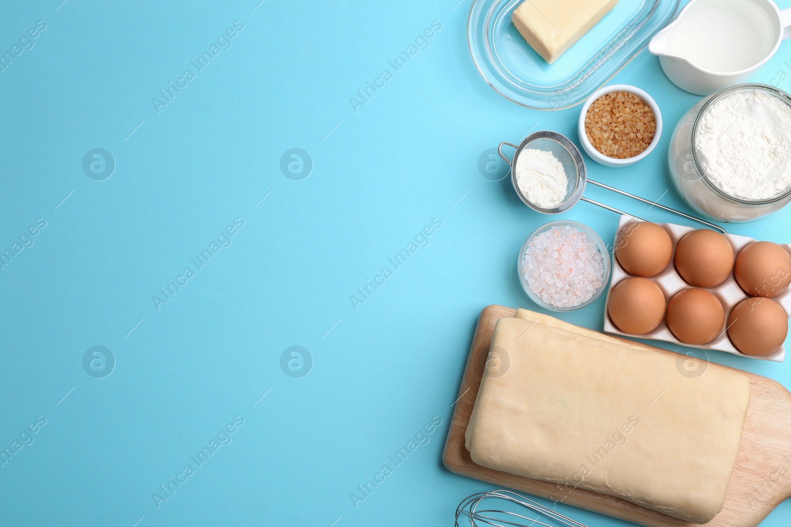 Photo of Puff pastry dough and ingredients on light blue background, flat lay. Space for text