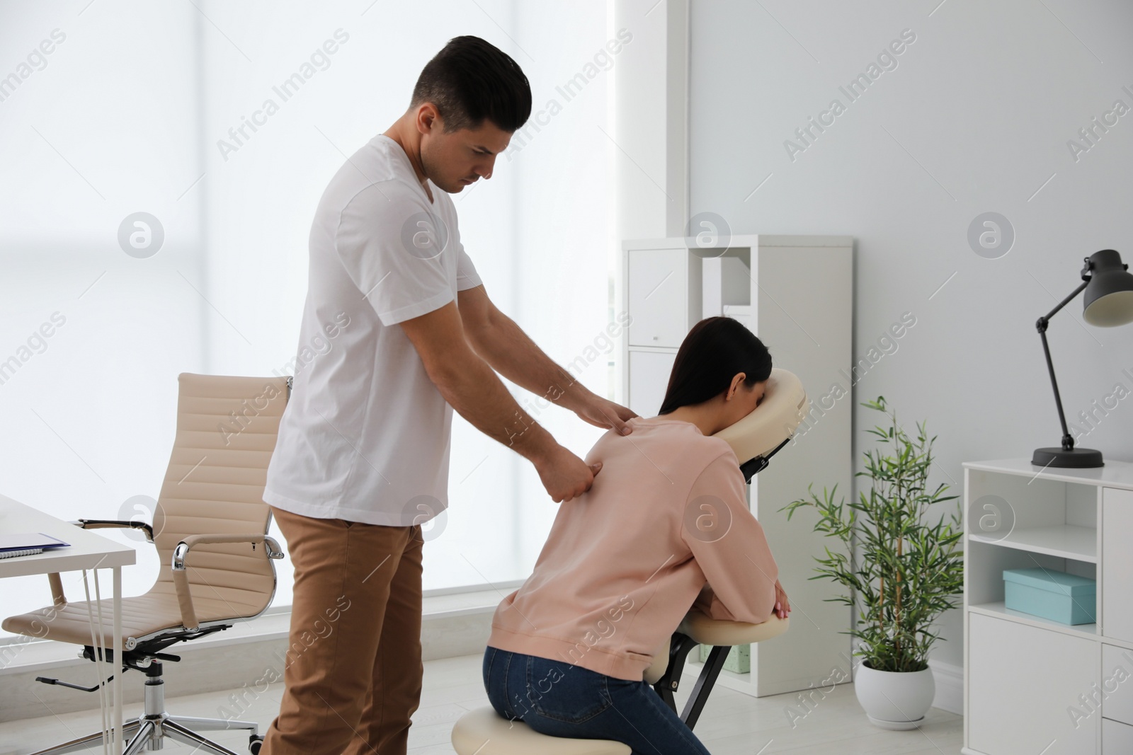 Photo of Woman receiving massage in modern chair indoors