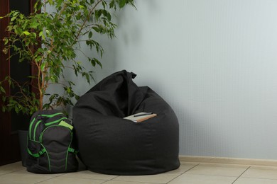 Black bean bag chair, houseplant and backpack near light grey wall in room. Space for text