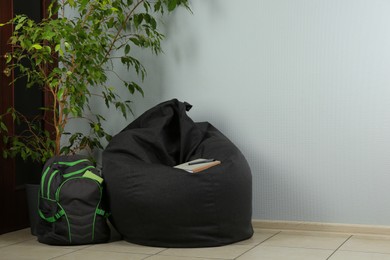 Photo of Black bean bag chair, houseplant and backpack near light grey wall in room. Space for text