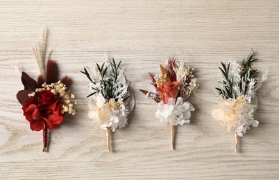Stylish boutonnieres on white wooden table, flat lay