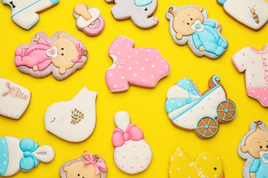 Cute tasty cookies of different shapes on yellow background, flat lay. Baby shower party