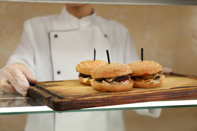 Photo of School canteen worker with burgers at serving line, closeup. Tasty food