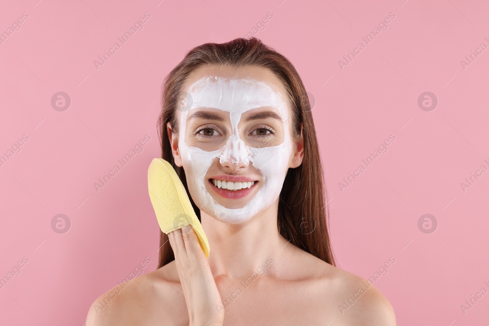 Photo of Happy young woman with face mask and sponge on pink background