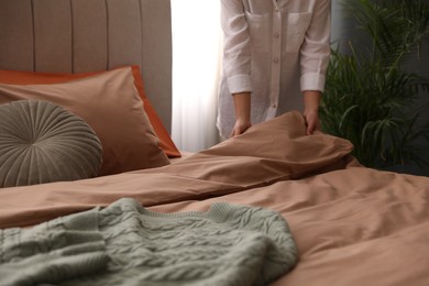 Photo of Woman making bed with stylish linens in room, closeup