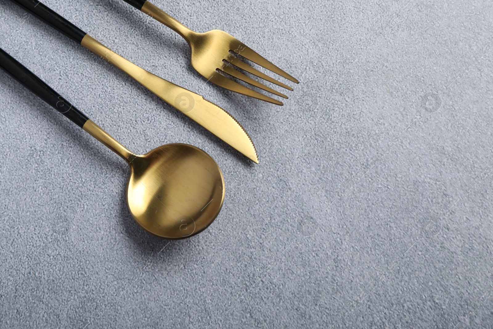 Photo of Stylish golden cutlery on grey table, above view. Space for text