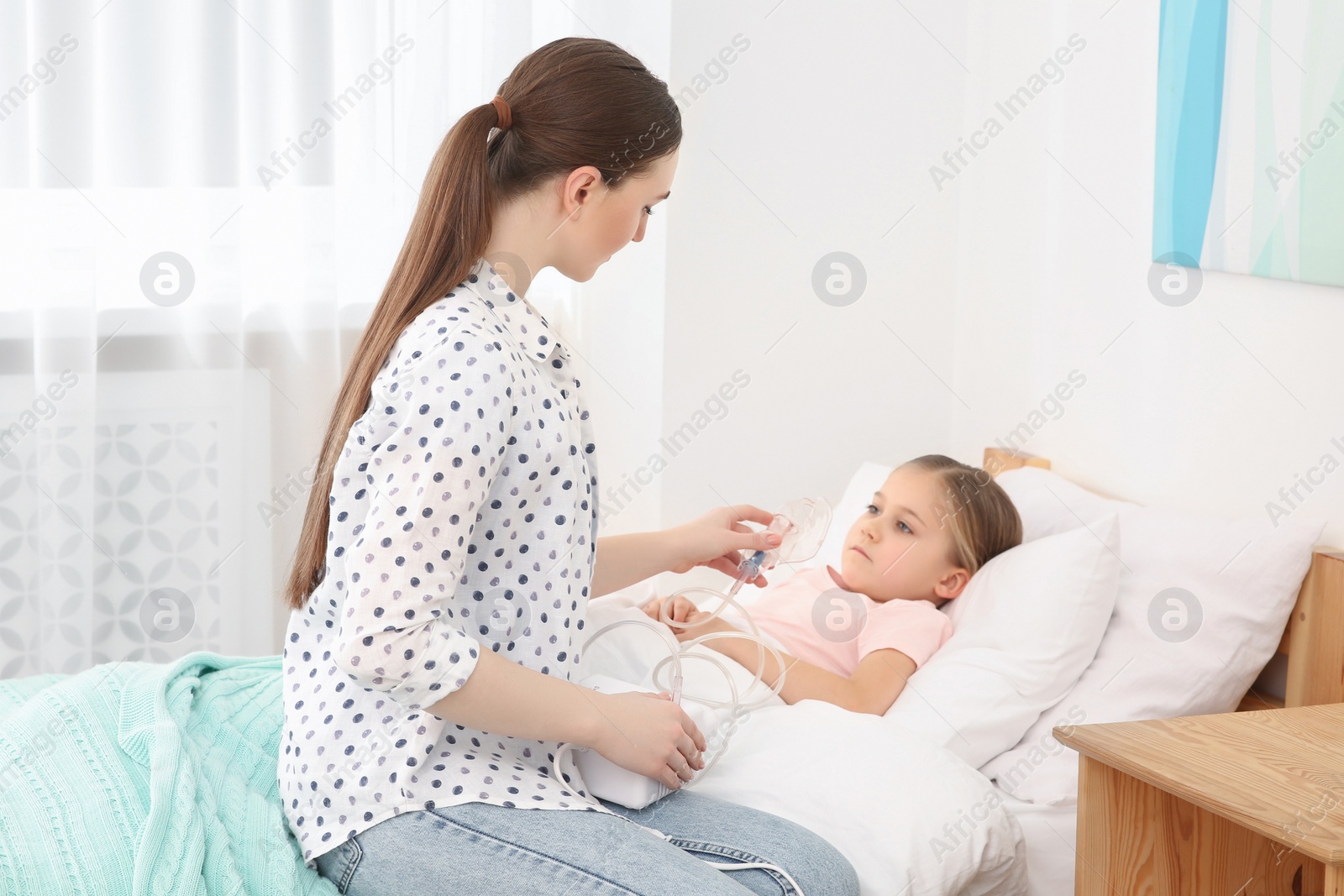 Photo of Mother helping her sick daughter with nebulizer inhalation in bedroom