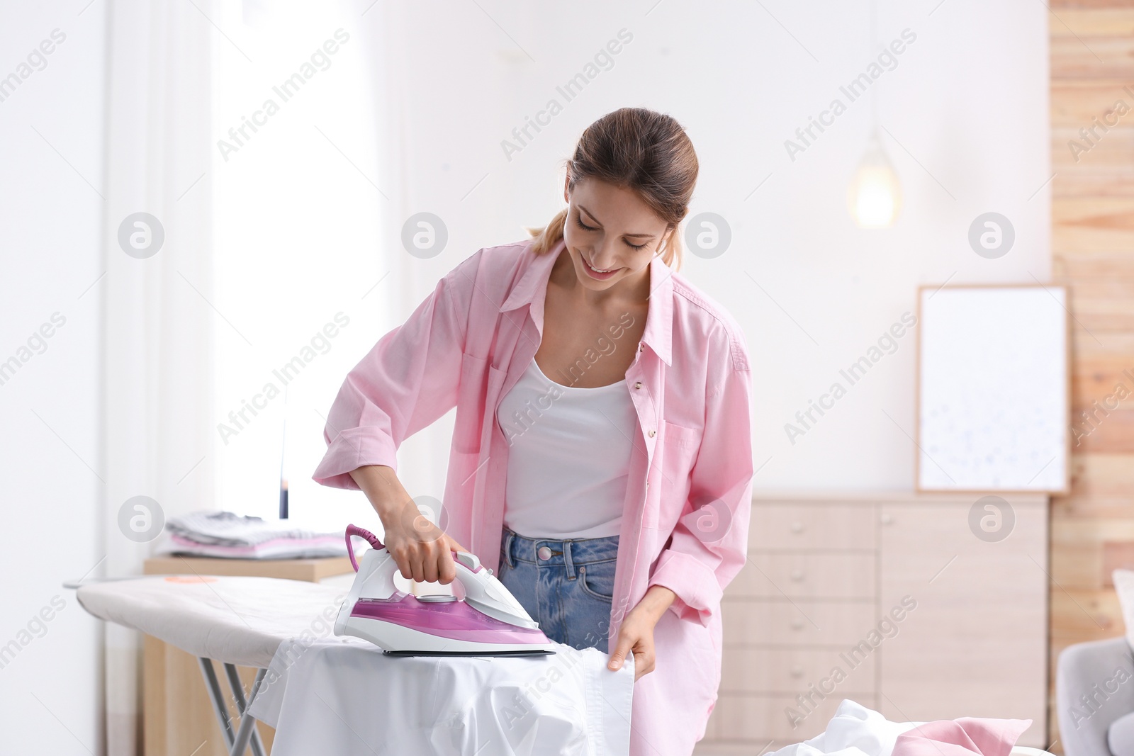 Photo of Young pretty woman ironing clean laundry indoors