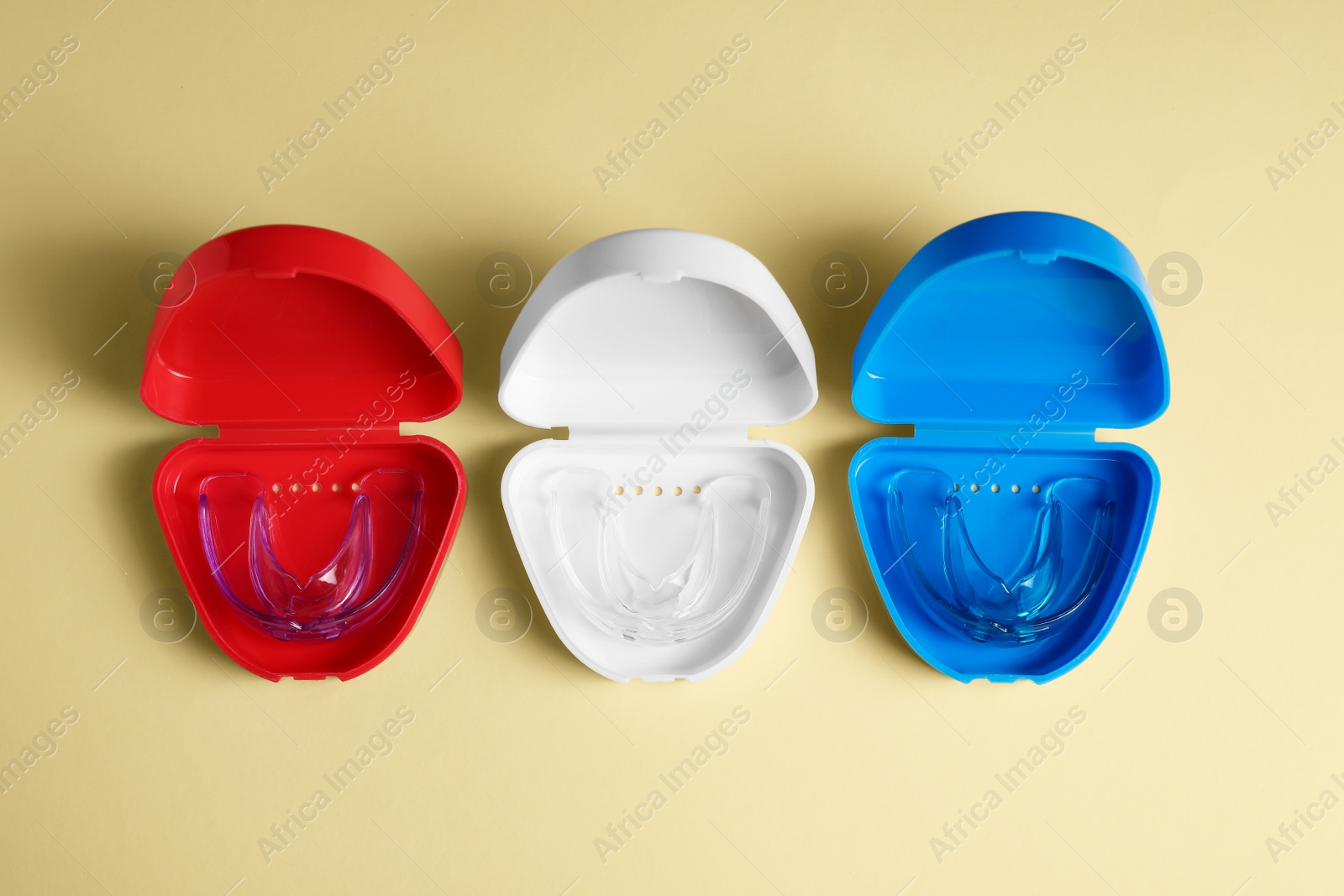 Photo of Transparent dental mouth guards in containers on beige background, flat lay. Bite correction