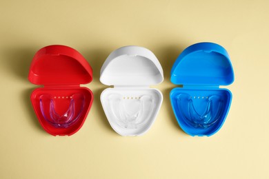 Photo of Transparent dental mouth guards in containers on beige background, flat lay. Bite correction