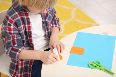 Photo of Boy using glue stick at desk in room, closeup. Home workplace