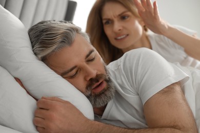 Photo of Irritated woman near her snoring husband in bed at home