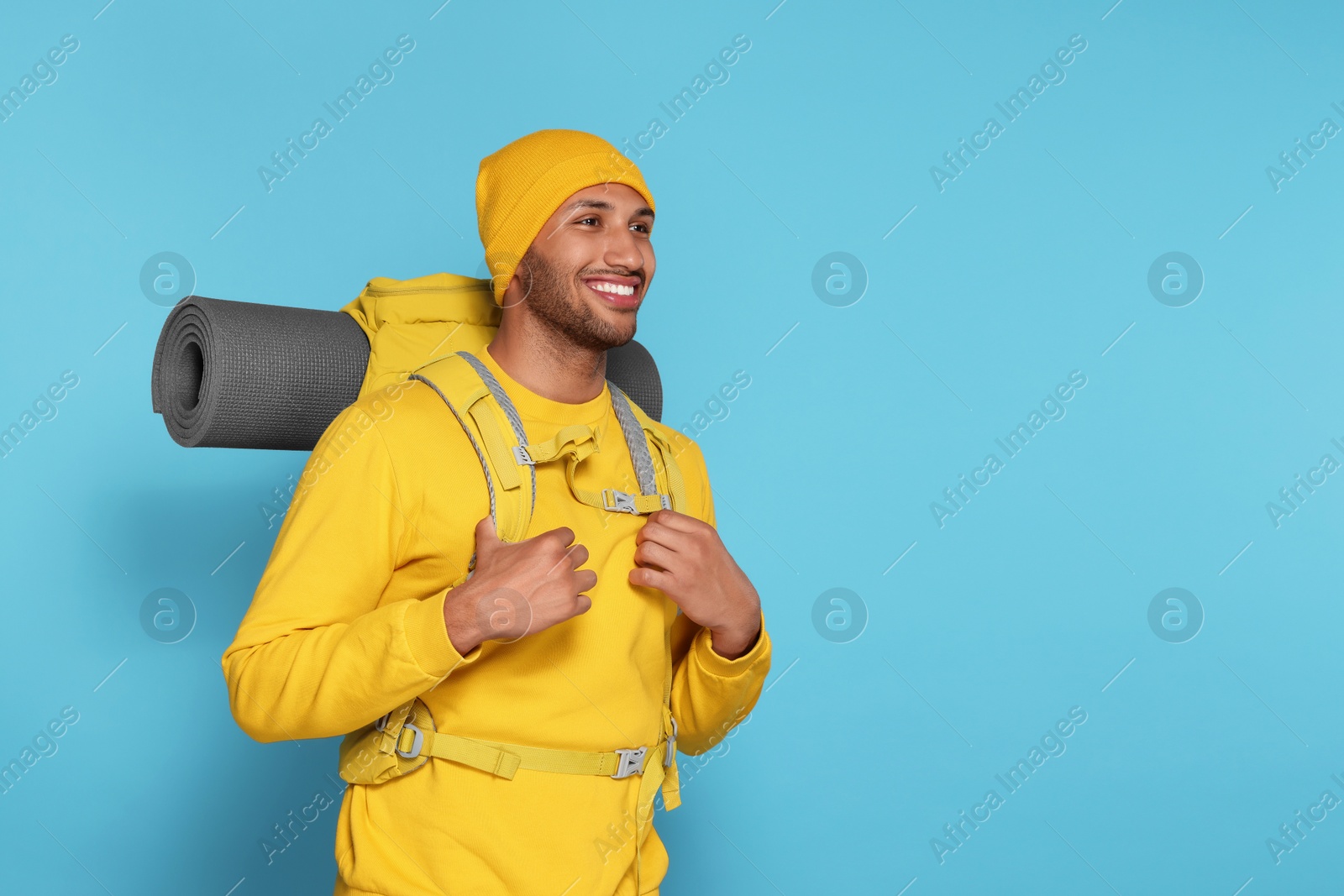 Photo of Happy tourist with backpack on light blue background, space for text