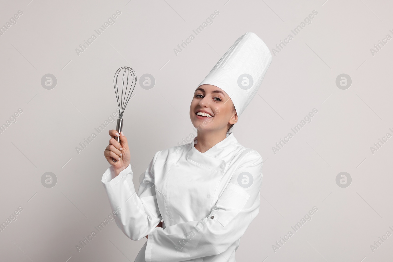 Photo of Happy professional confectioner in uniform holding whisk on light grey background