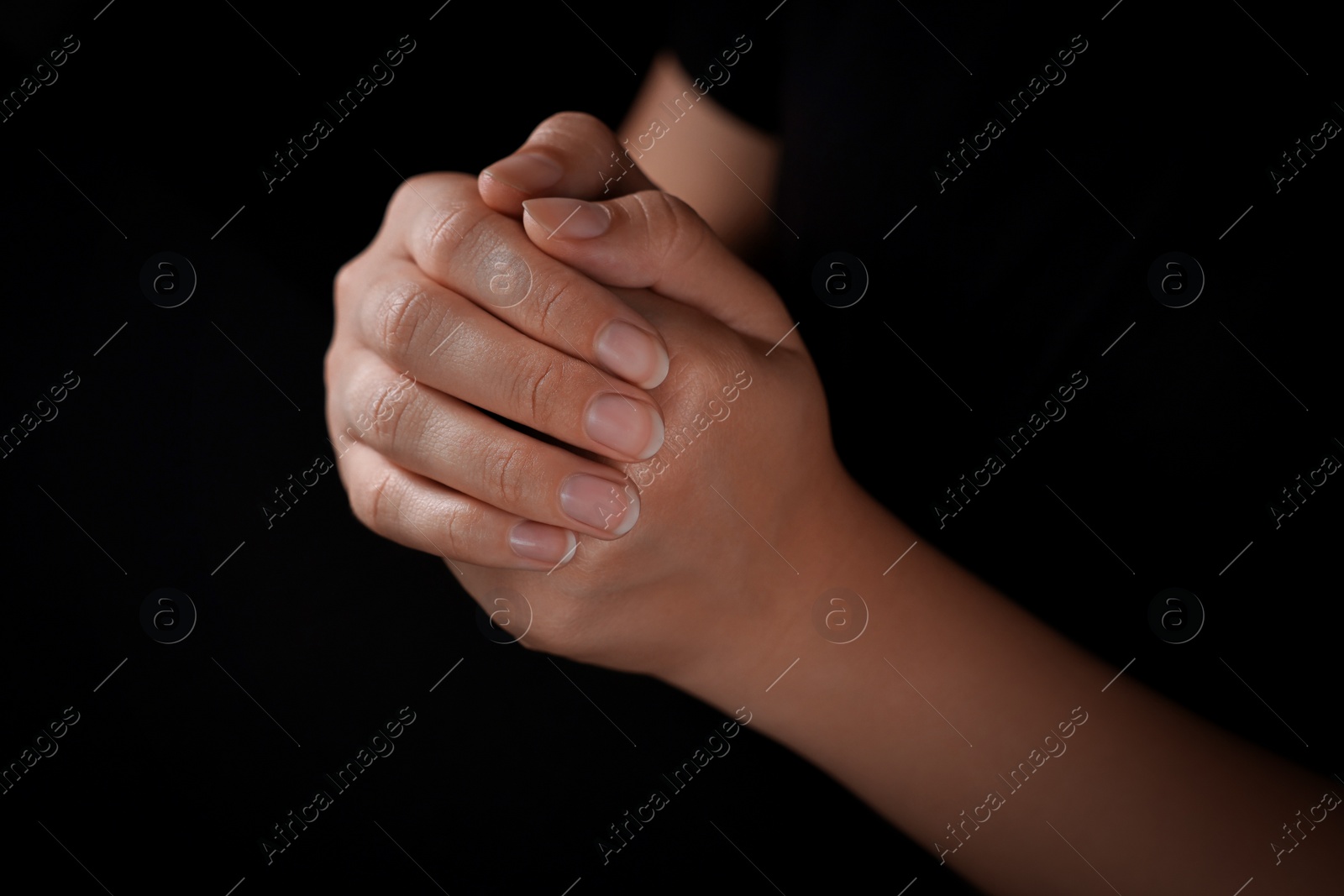 Photo of Woman holding hands clasped while praying against black background, closeup