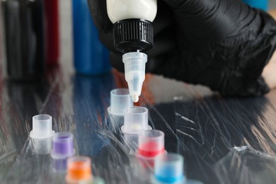 Photo of Tattoo artist dripping white tattoo ink into cap on table, closeup