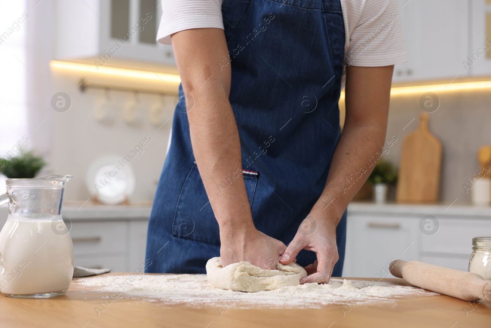 Photo of Making bread. Man kneading dough at wooden table in kitchen, closeup