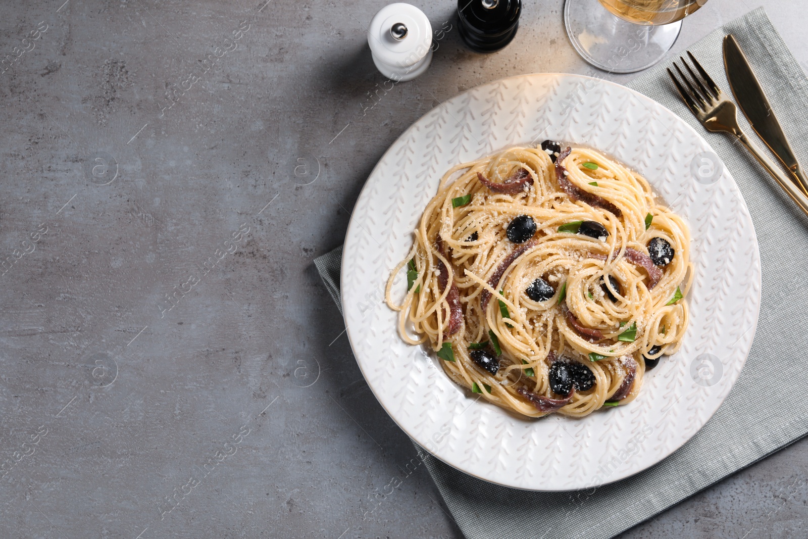 Photo of Delicious pasta with anchovies, olives and parmesan cheese served on grey table, flat lay. Space for text