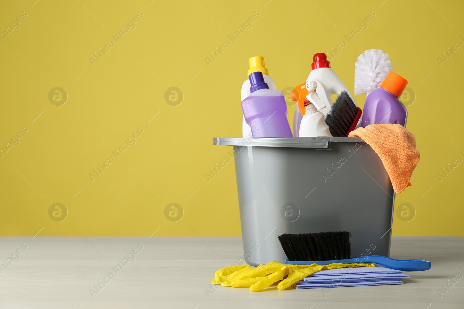 Photo of Bucket with cleaning products and tools on grey table. Space for text