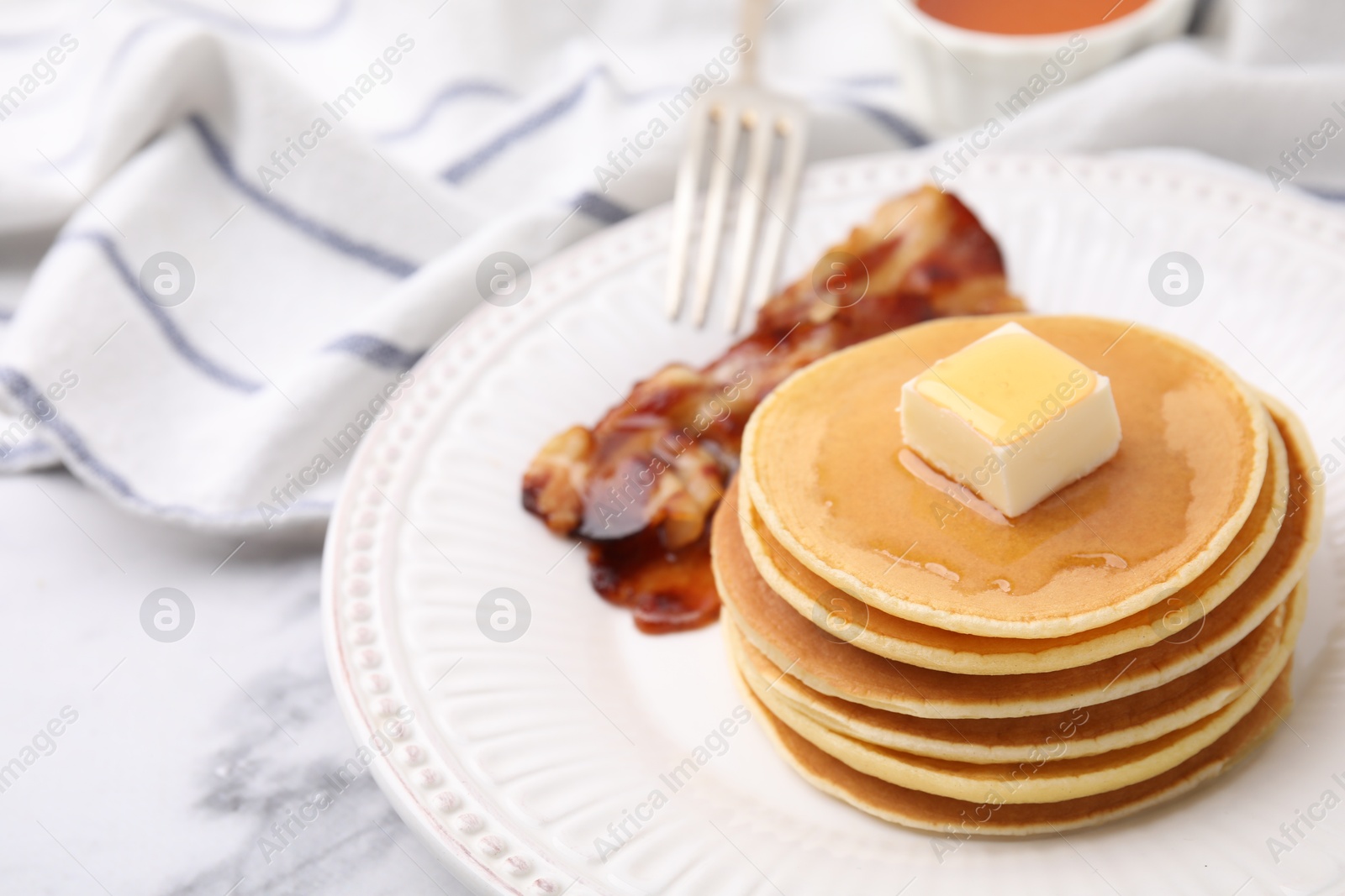 Photo of Delicious pancakes with butter, maple syrup and fried bacon on white marble table