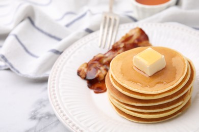 Delicious pancakes with butter, maple syrup and fried bacon on white marble table