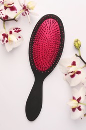 Photo of Stylish hairbrush and orchid flowers on white background, top view