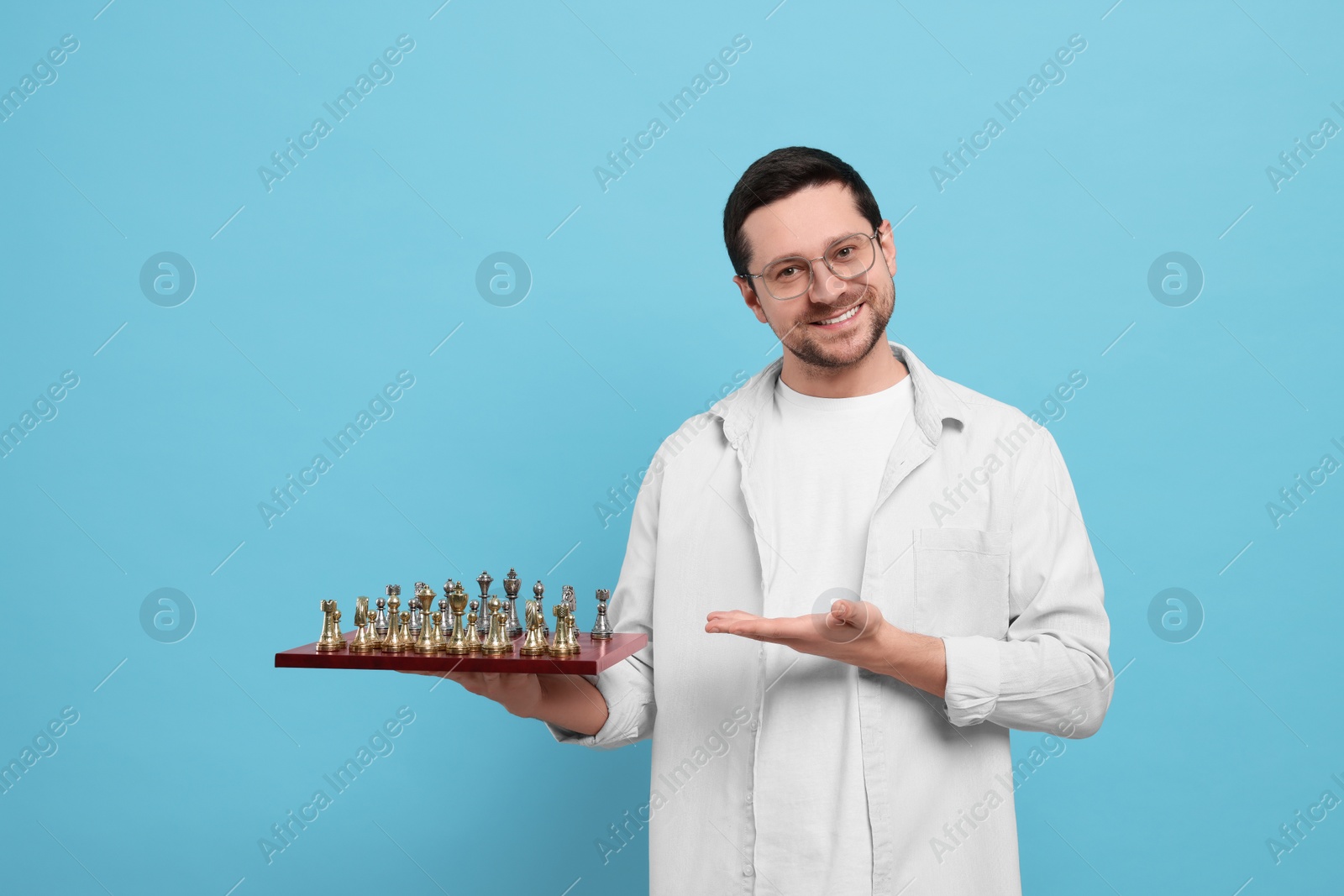 Photo of Handsome man showing chessboard with game pieces on light blue background