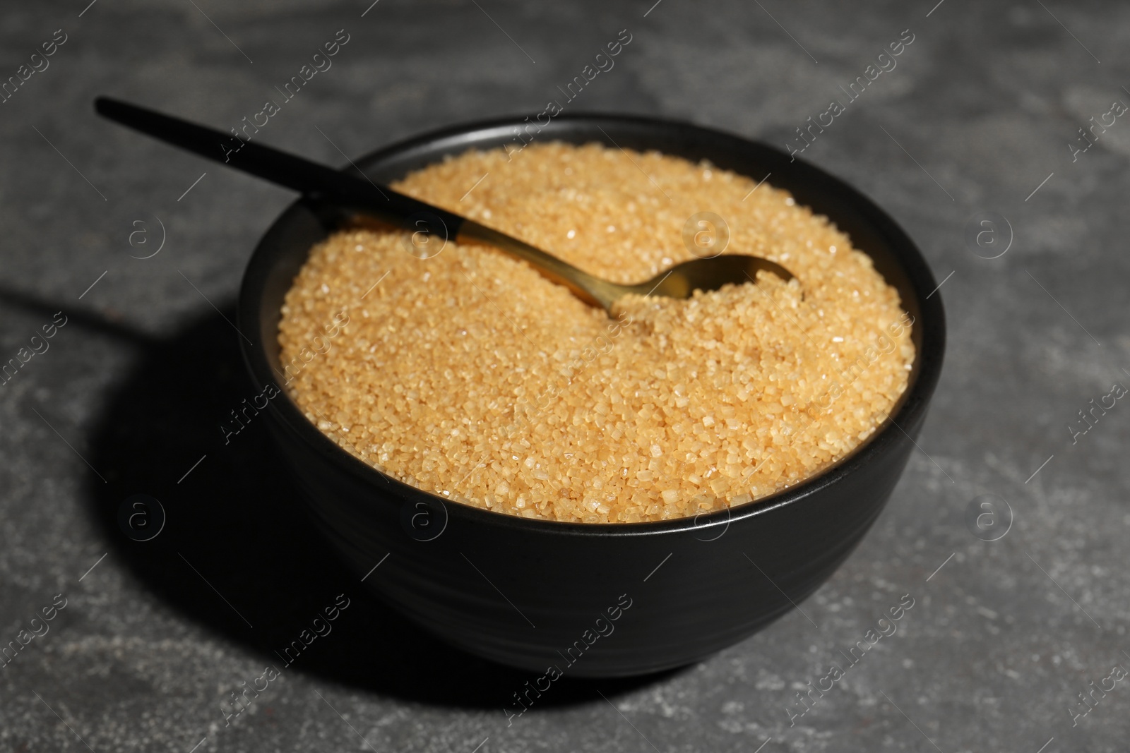 Photo of Brown sugar in bowl and spoon on grey textured table, closeup