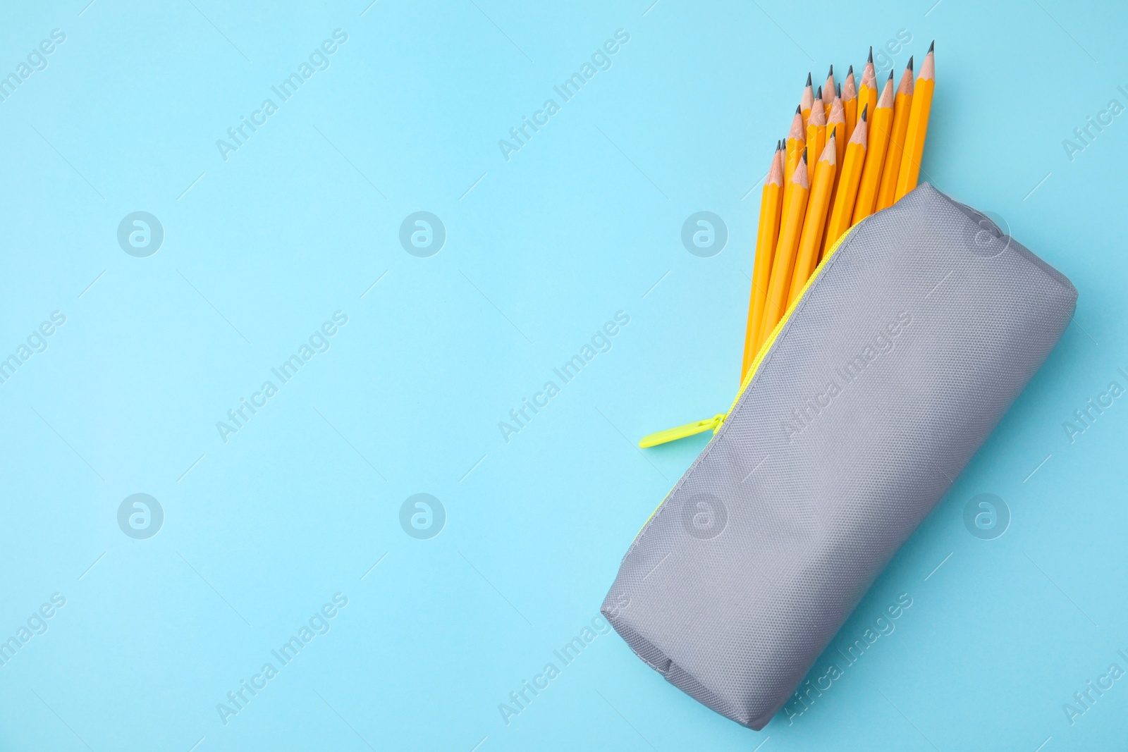 Photo of Many sharp pencils in pencil case on light blue background, top view. Space for text